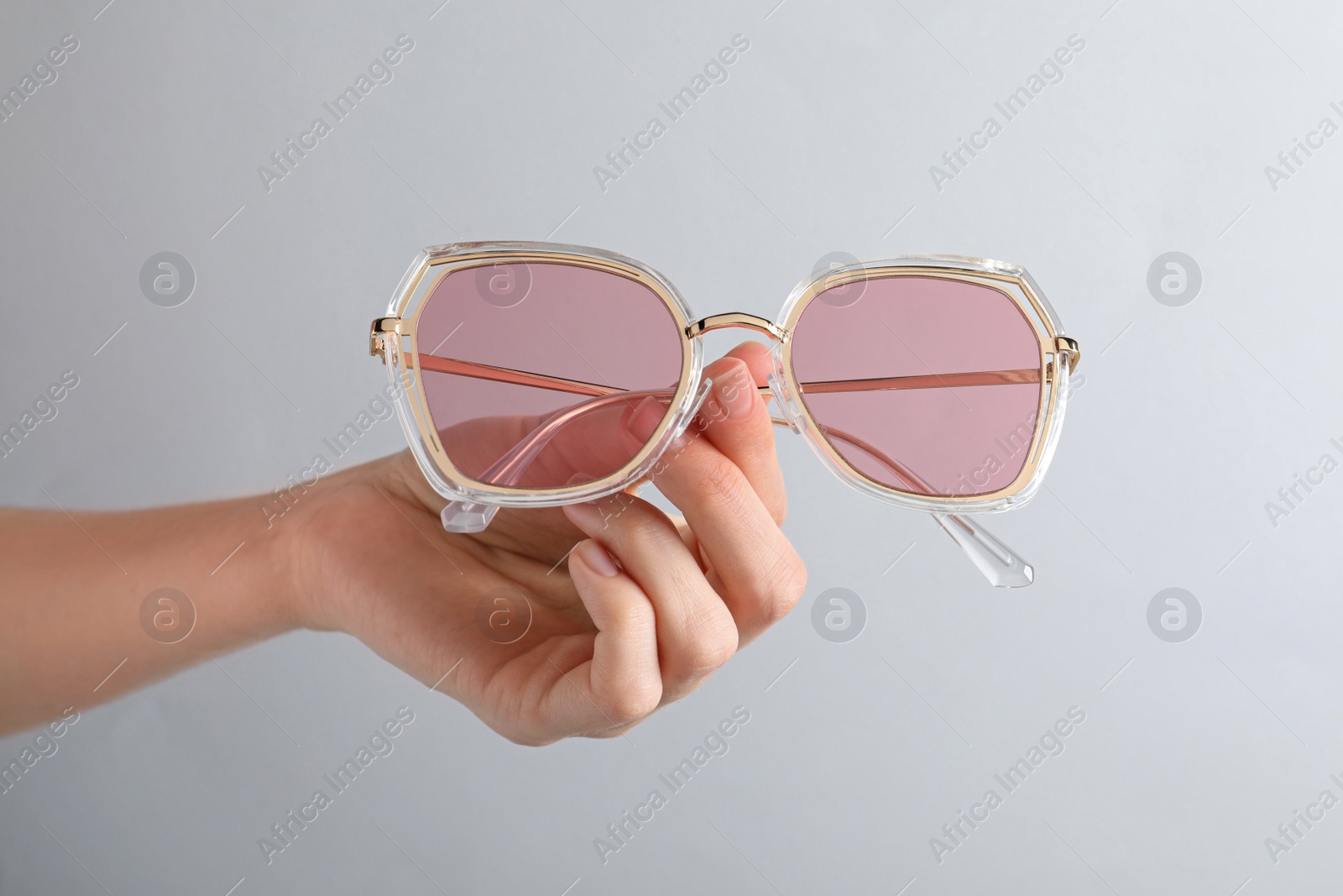 Photo of Woman holding stylish sunglasses on light grey background, closeup of hand