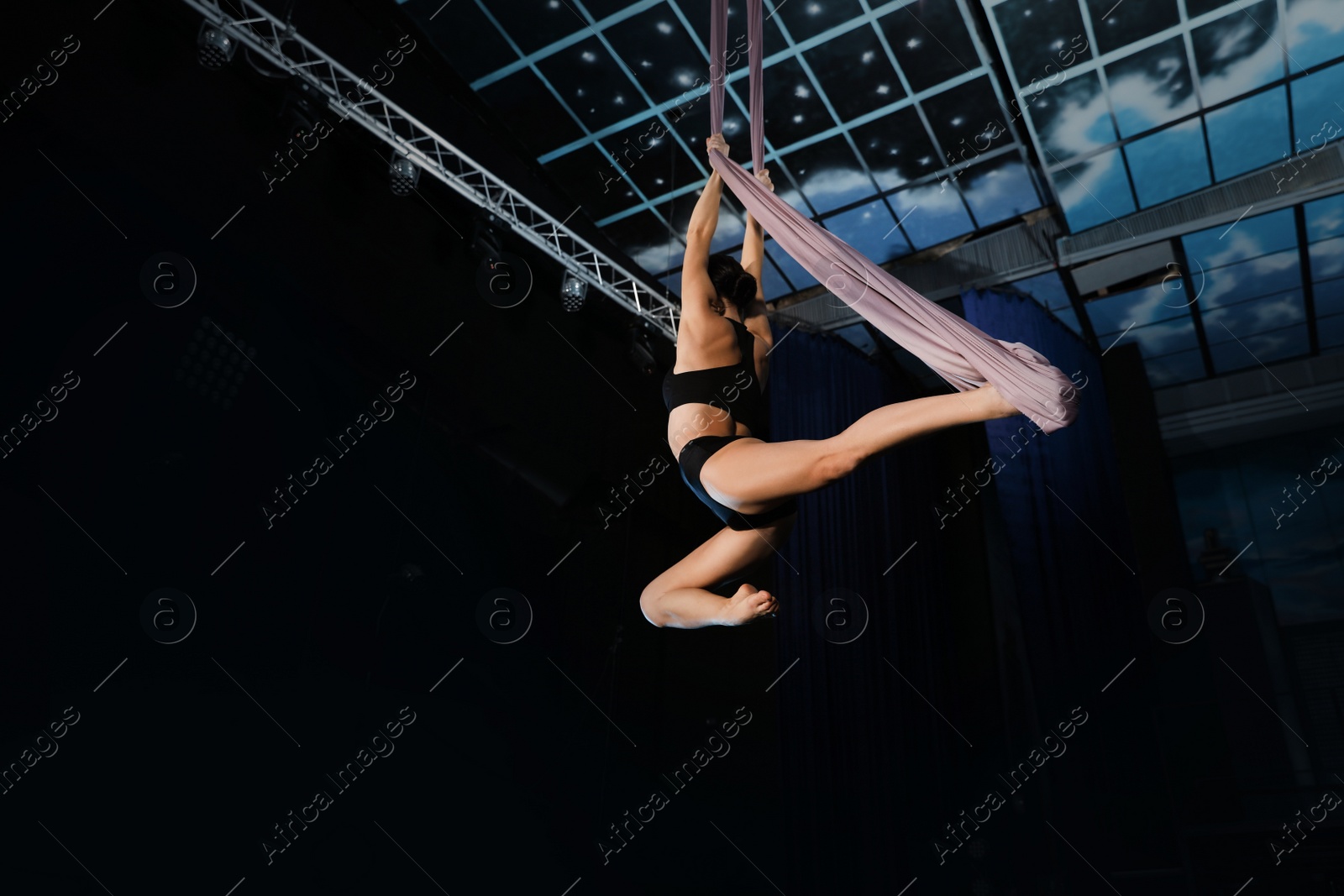 Photo of Young woman performing acrobatic element on aerial silk indoors