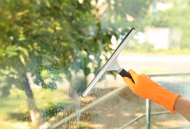 Photo of Janitor cleaning window with squeegee indoors, closeup