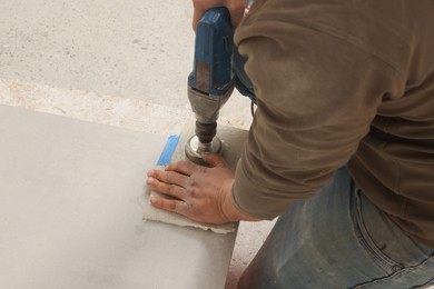 Photo of Worker with electric drill preparing tiles for installation indoors, closeup