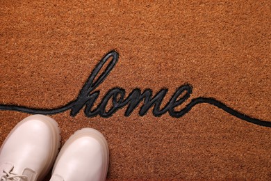 Photo of Stylish boots on doormat with word Home, top view