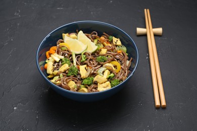 Photo of Stir-fry. Delicious cooked noodles with chicken and vegetables in bowl served on gray textured table