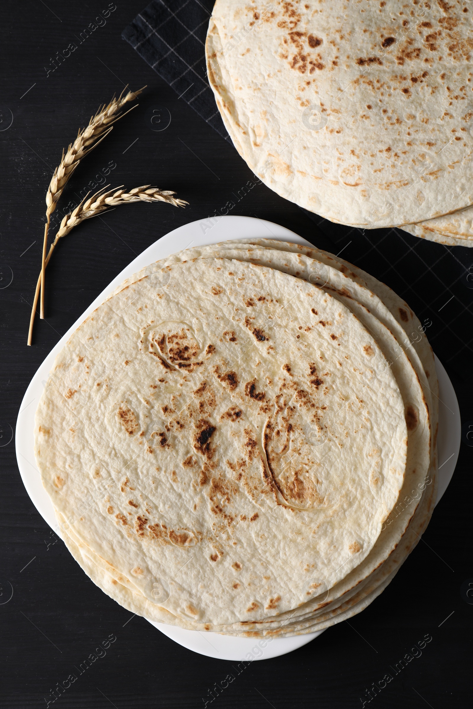 Photo of Many tasty homemade tortillas on black wooden table, top view