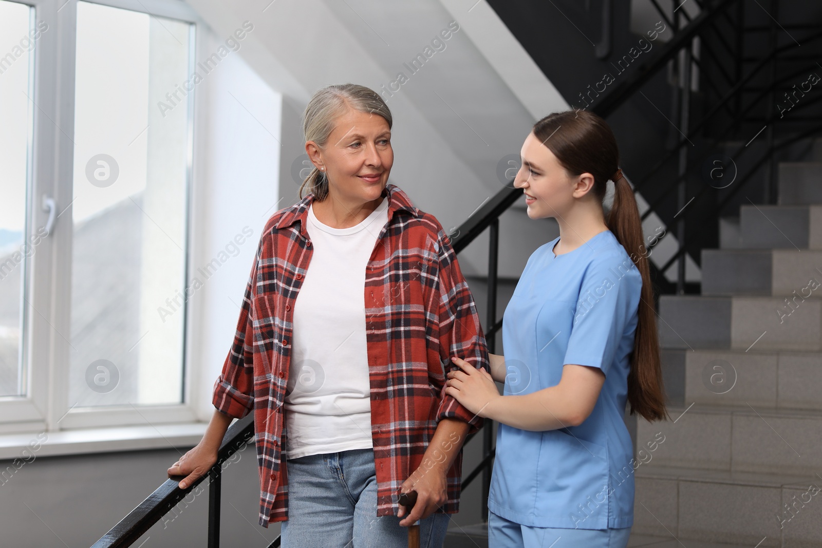 Photo of Young healthcare worker assisting senior woman on stairs indoors