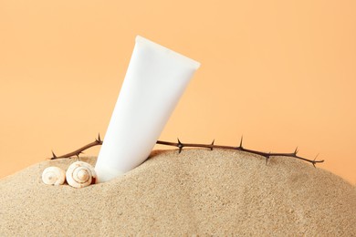 Photo of Tube with cream, shells and branches on sand against orange background. Cosmetic product