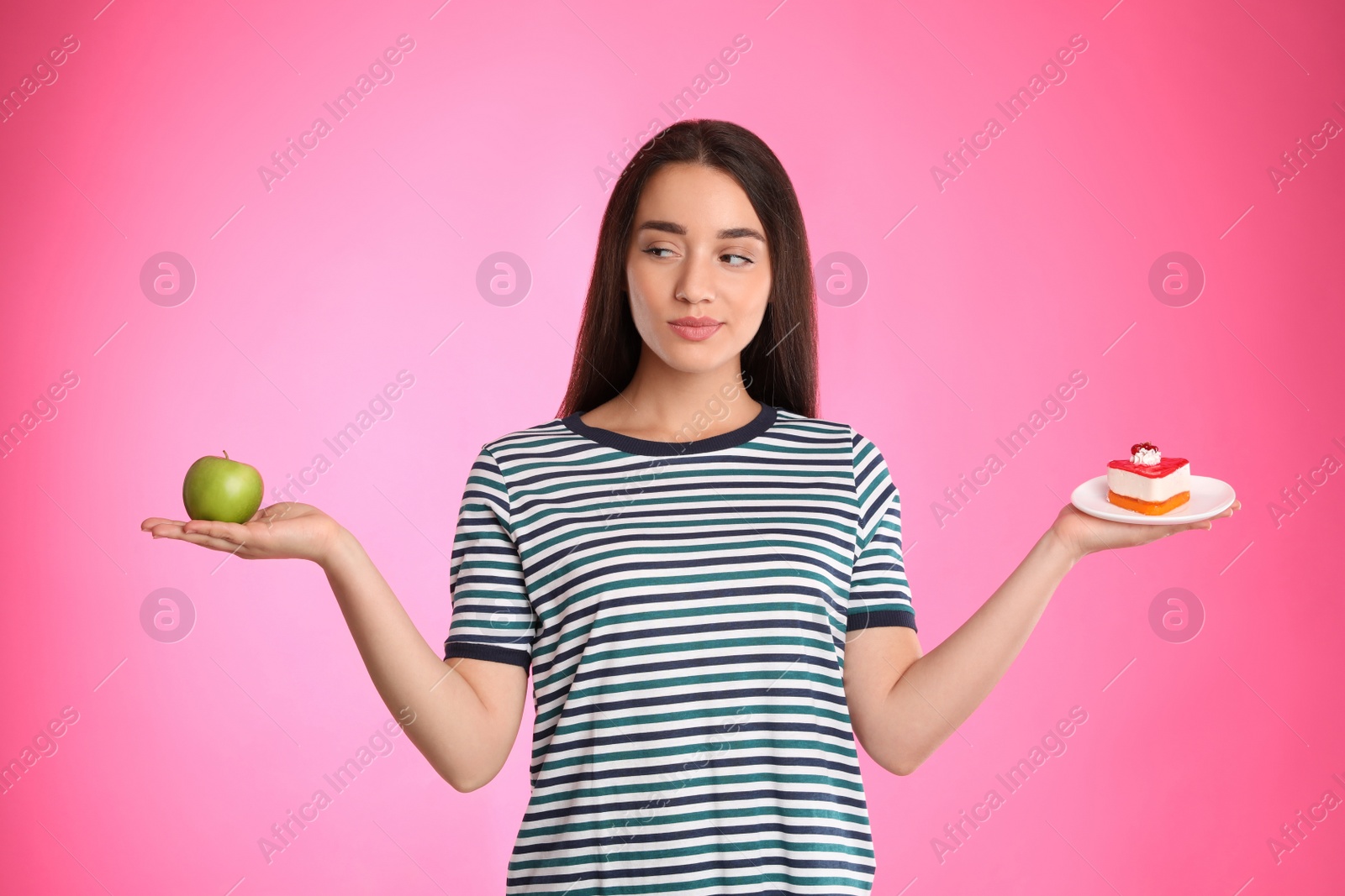 Photo of Concept of choice. Woman holding apple and cake on pink background