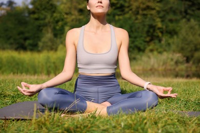 Woman practicing yoga on mat outdoors, closeup. Lotus pose