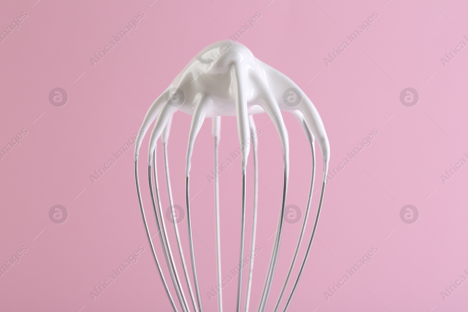 Photo of Whisk with whipped cream on pink background, closeup