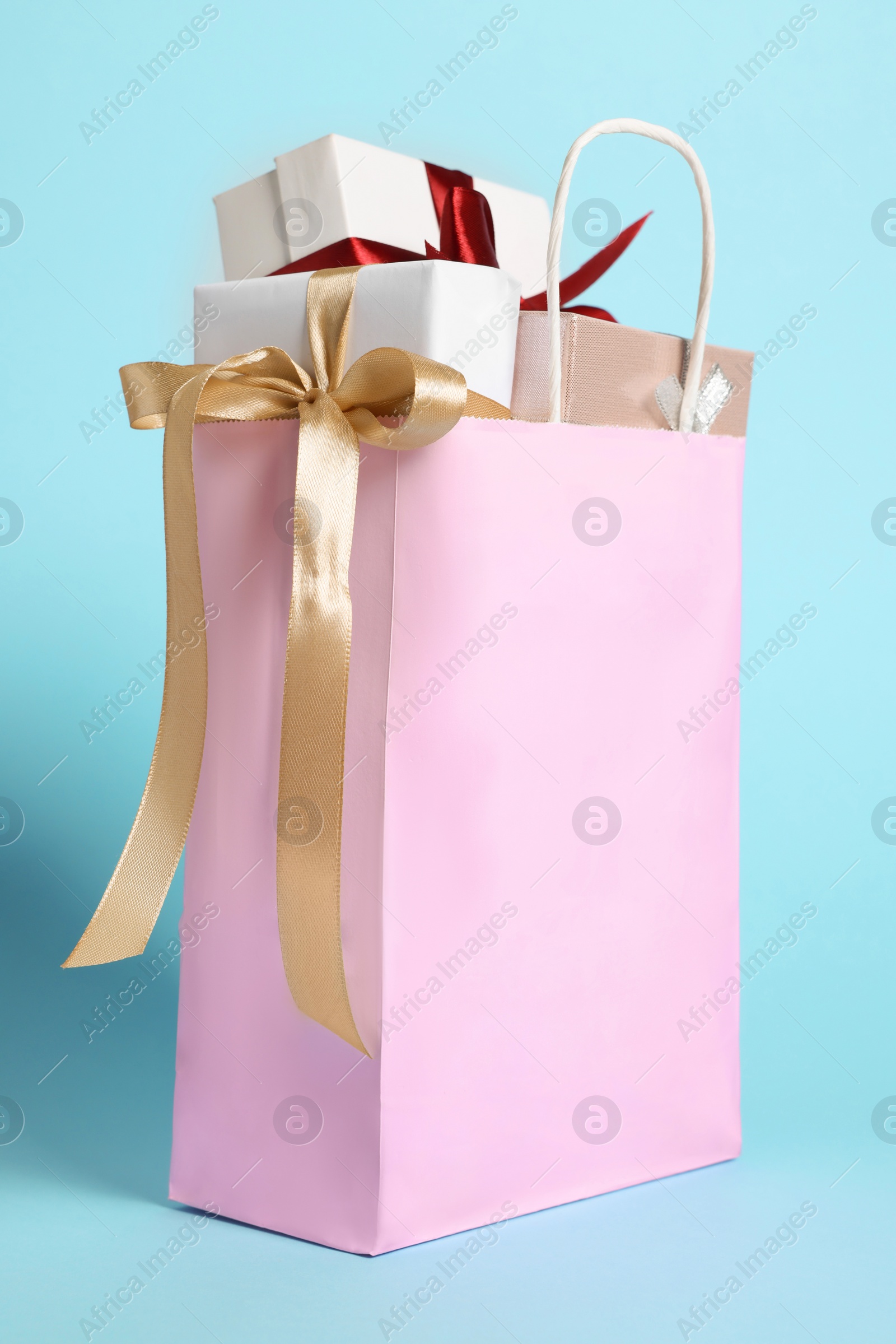 Photo of Pink paper shopping bag full of gift boxes on light blue background