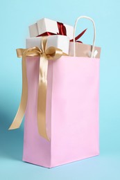 Photo of Pink paper shopping bag full of gift boxes on light blue background