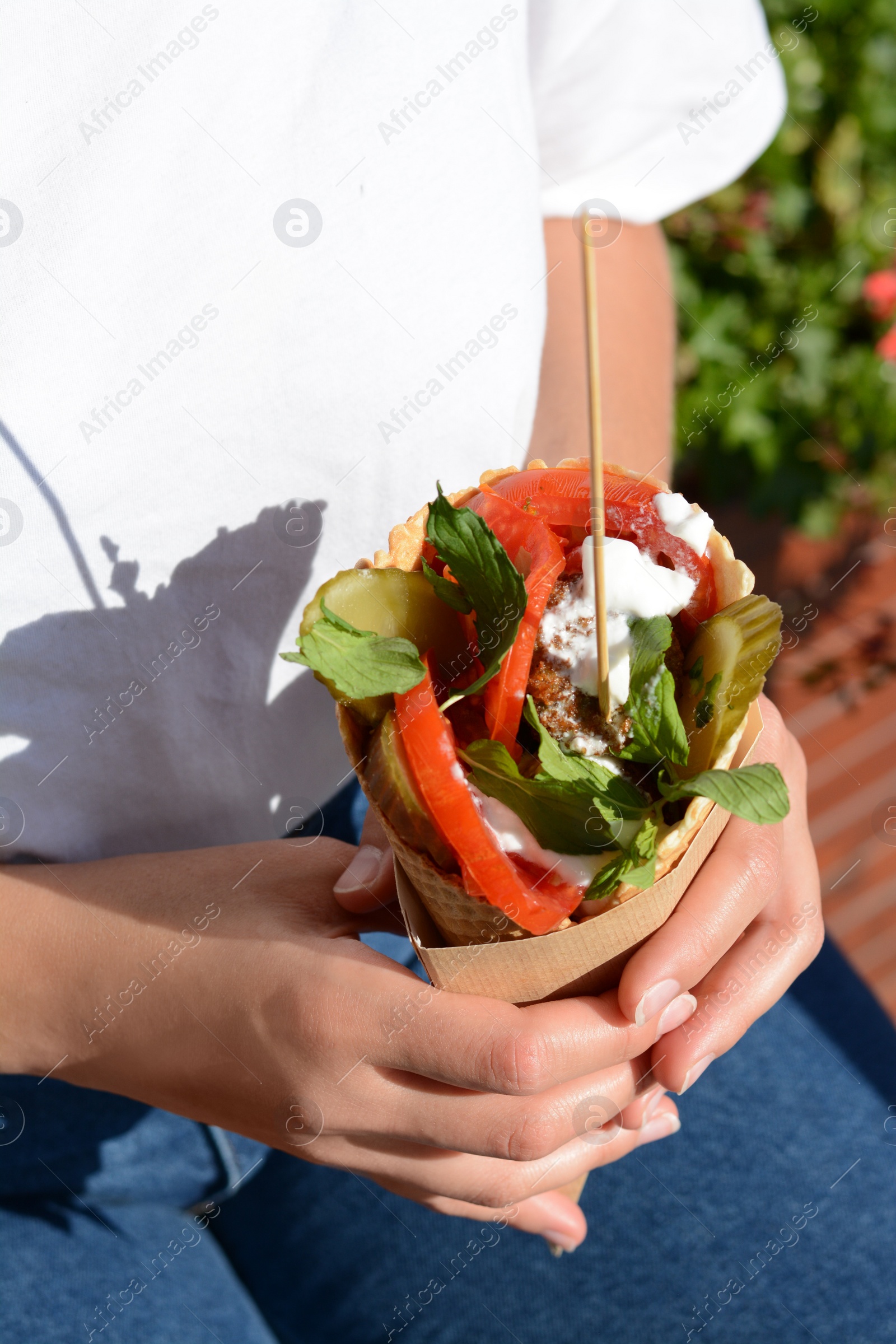 Photo of Woman holding wafer with falafel and vegetables outdoors, closeup. Street food