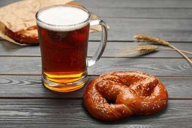Photo of Mug of beer with tasty freshly baked pretzel on grey wooden table