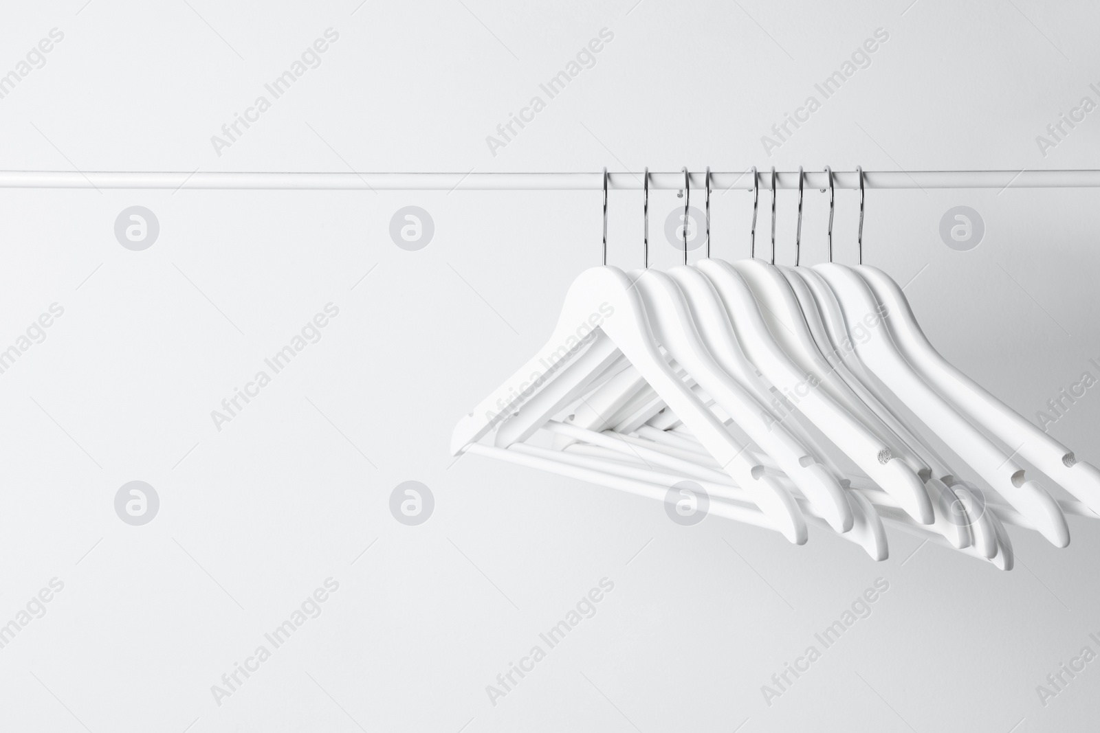 Photo of White clothes hangers on metal rail against light background. Space for text