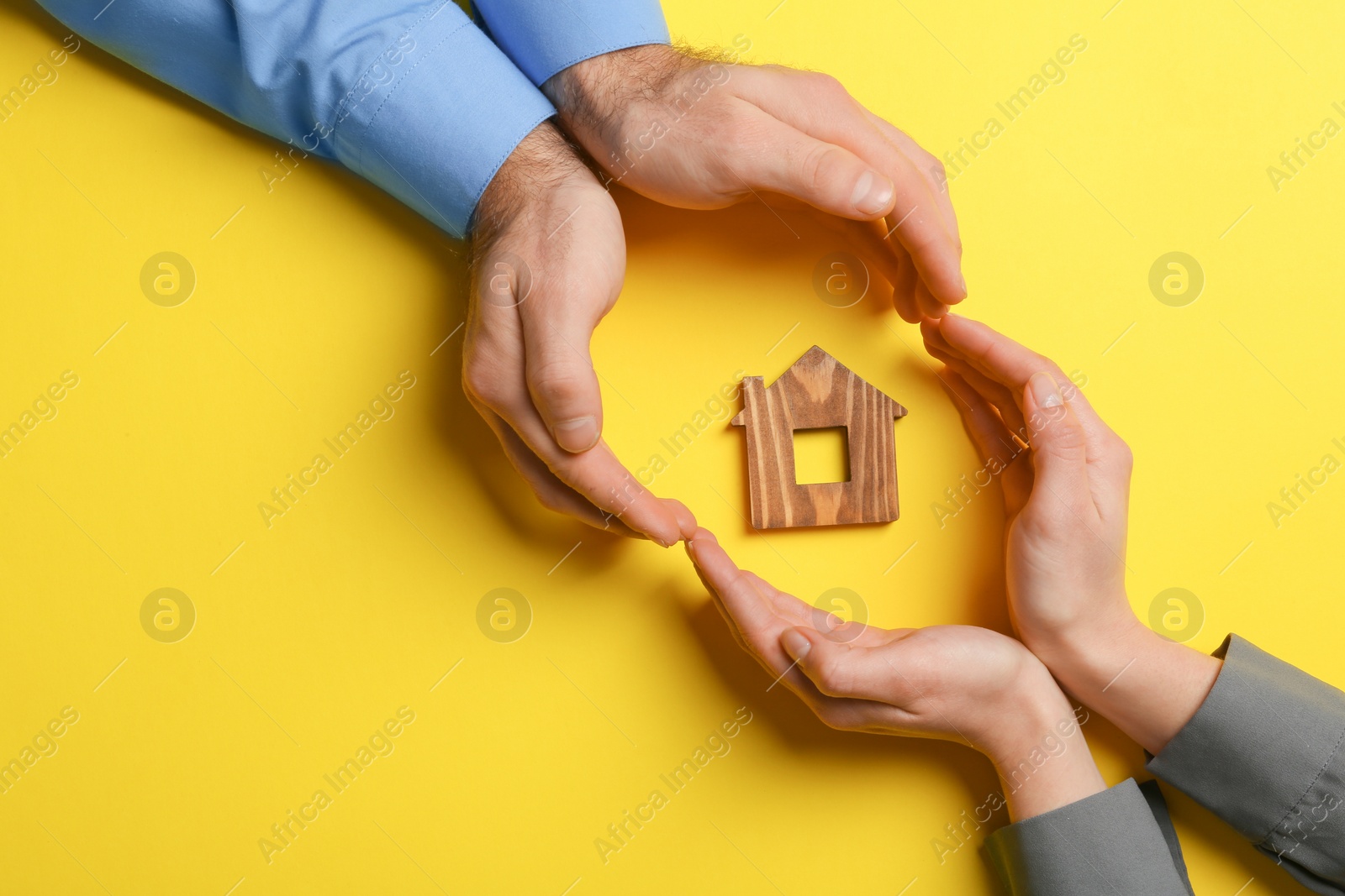 Photo of Couple holding hands near figure of house on color background, top view with space for text. Home insurance