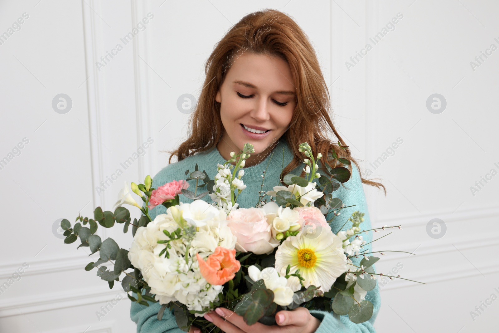 Photo of Beautiful woman with bouquet of flowers near white wall indoors