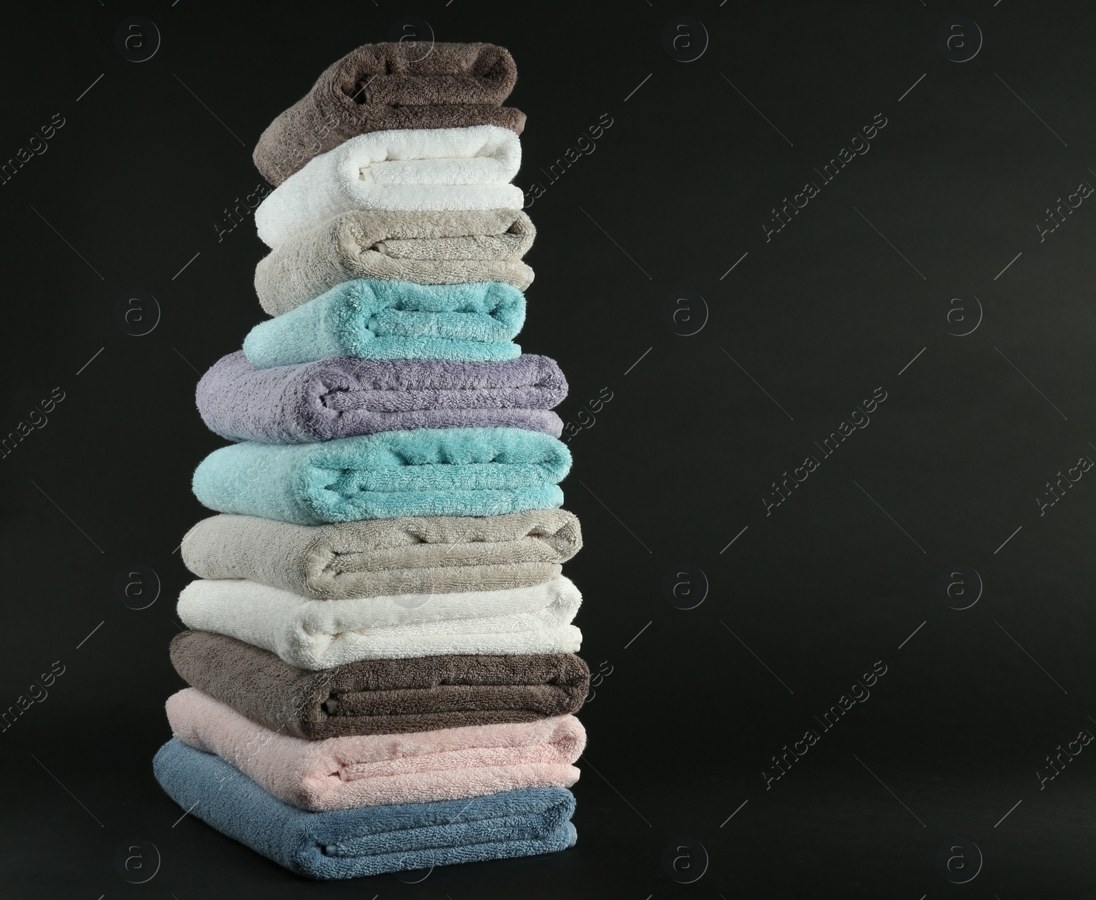 Photo of Different fresh soft terry towels on dark background. Space for text