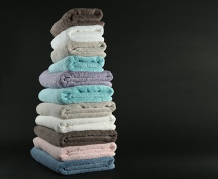 Photo of Different fresh soft terry towels on dark background. Space for text