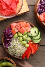 Delicious poke bowls with vegetables, fish and edamame beans on wooden table, flat lay