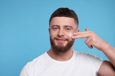 Photo of Handsome man applying cream onto his face on light blue background