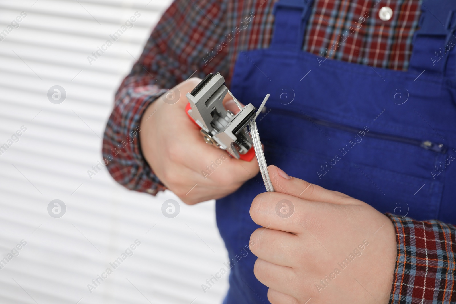 Photo of Professional electrician in uniform stripping wiring indoors, closeup