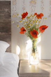 Photo of Glass vase with bouquet of beautiful wildflowers on nightstand in bedroom