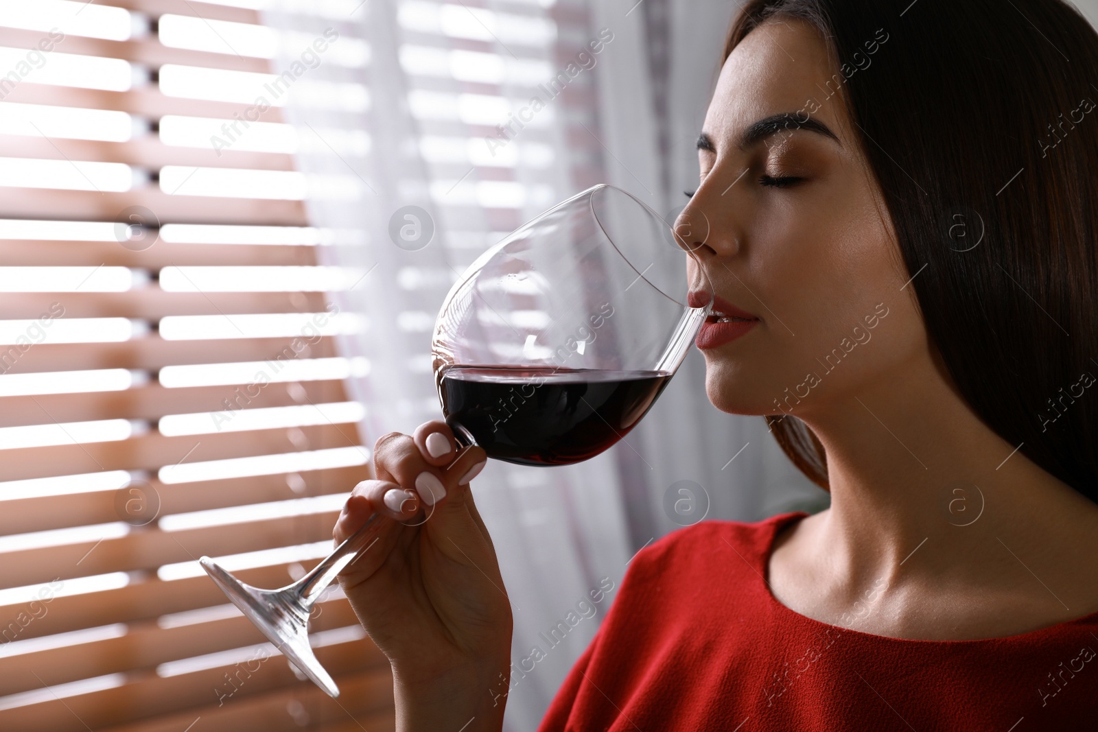 Photo of Beautiful young woman with glass of luxury red wine indoors. Space for text