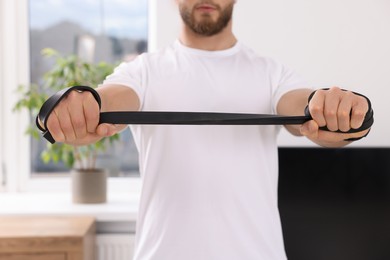 Athletic man doing exercise with elastic resistance band indoors, closeup