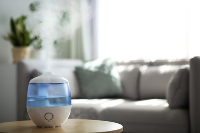 Modern air humidifier on table in living room. Space for text