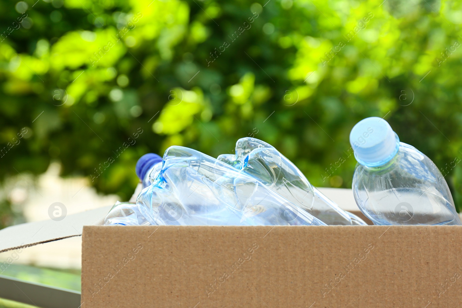 Photo of Cardboard box with used plastic bottles outdoors. Recycle concept