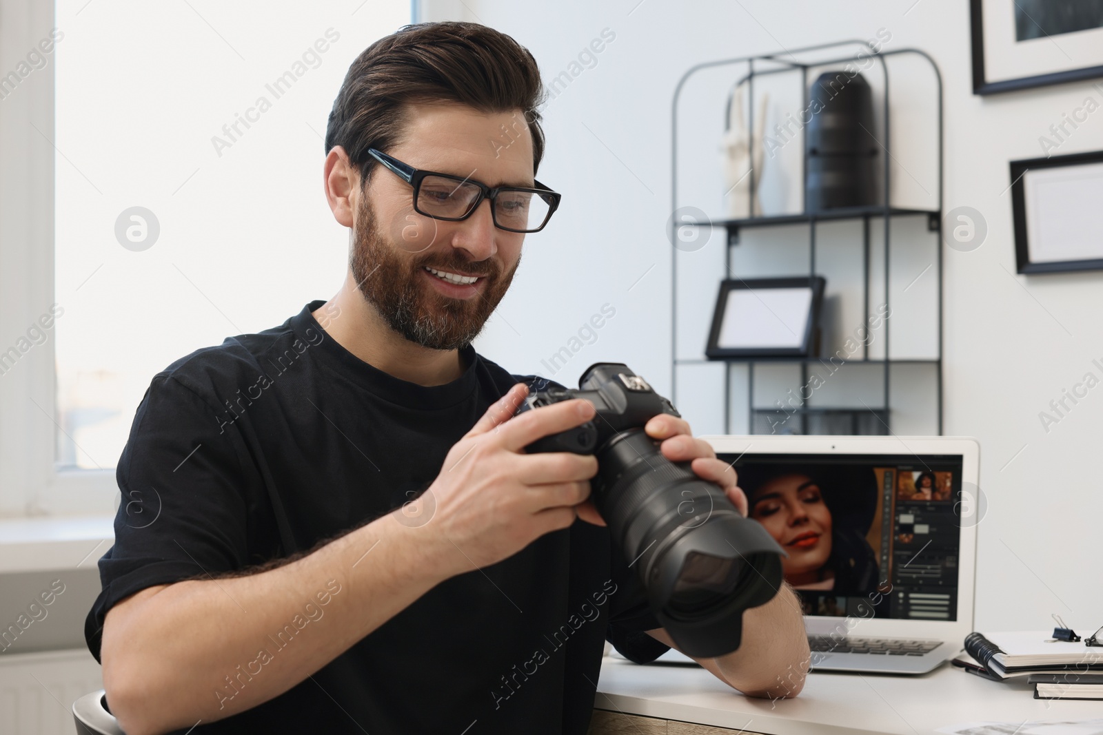 Photo of Professional photographer in glasses holding digital camera at table in office