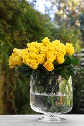 Photo of Beautiful bouquet of yellow roses in glass vase on light table outdoors