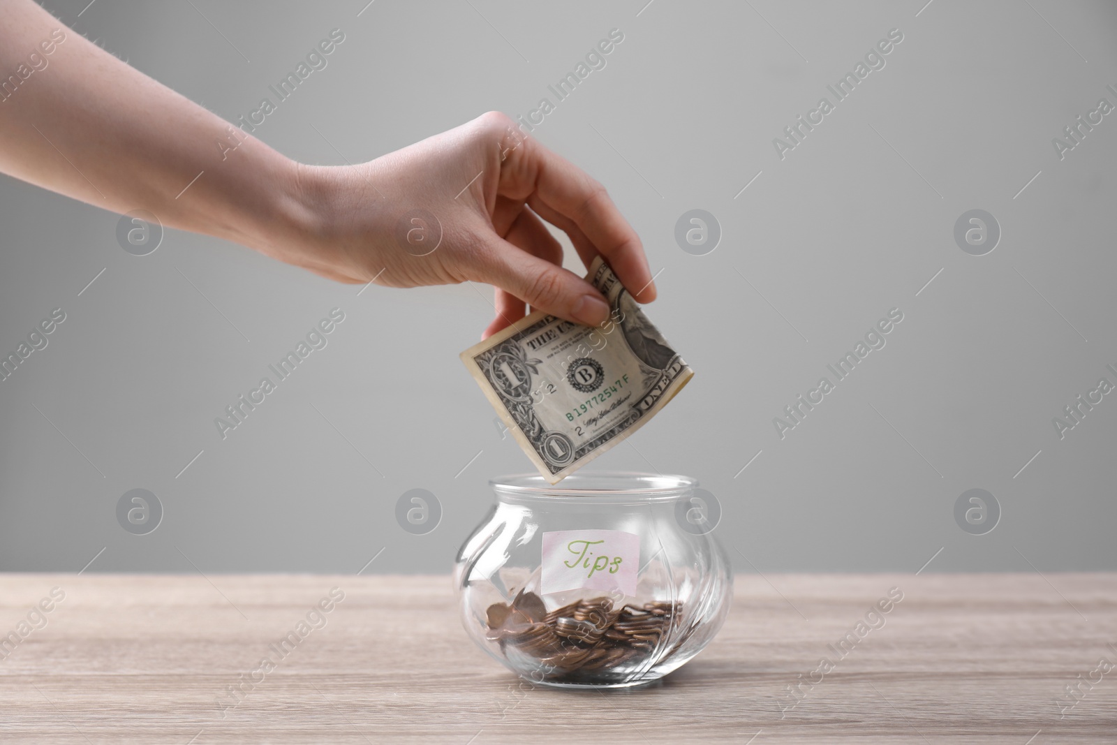 Photo of Woman putting tips into glass vase on wooden table, closeup