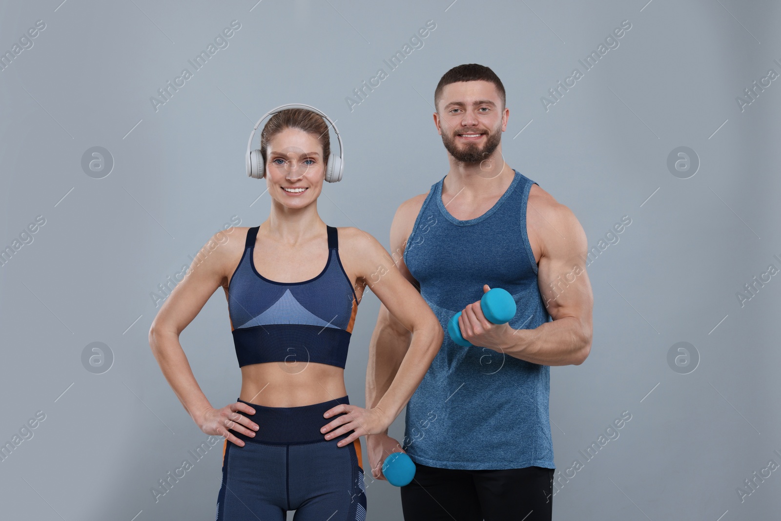 Photo of Athletic people with dumbbells and headphones on grey background
