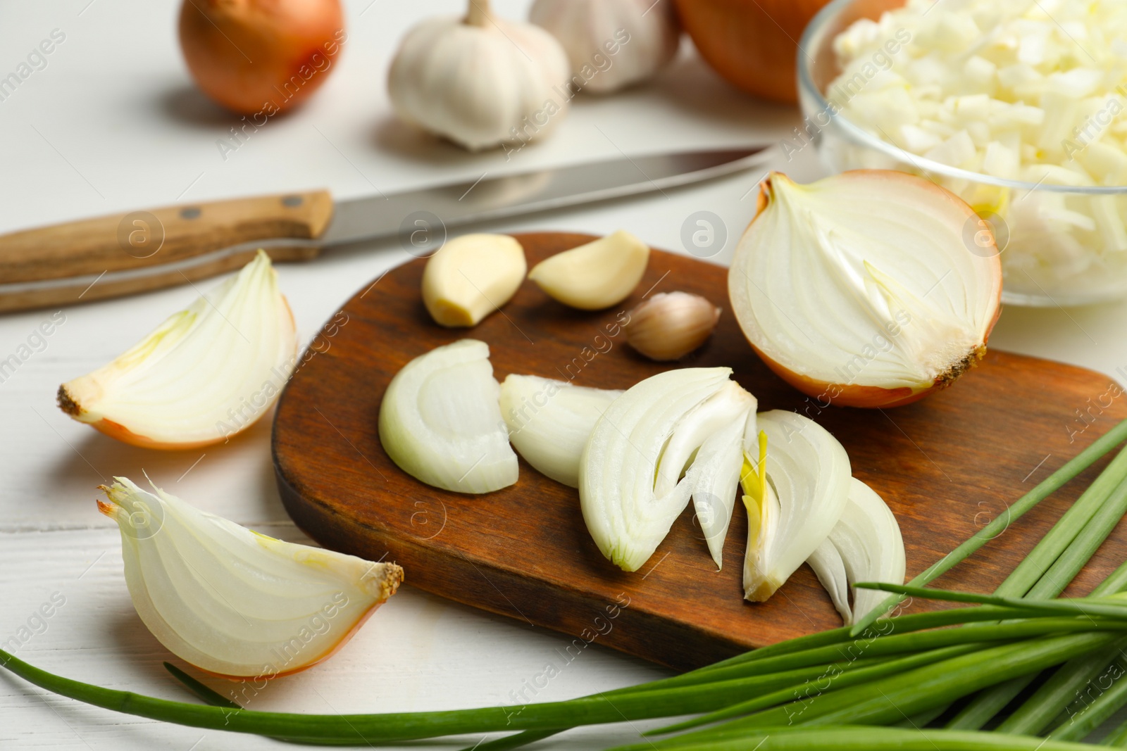 Photo of Board with cut onion and garlic on white wooden table
