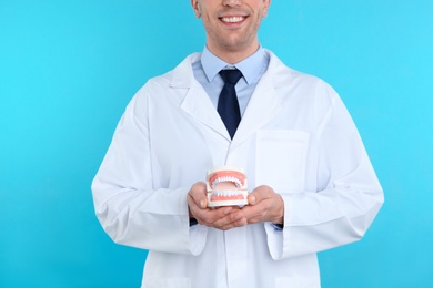 Photo of Male dentist holding jaws model on color background
