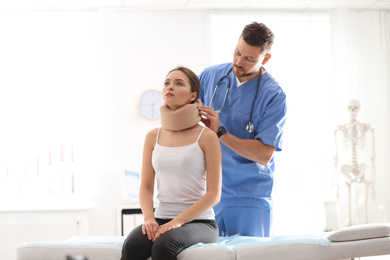 Male orthopedist applying cervical collar onto patient's neck in clinic