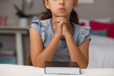 Photo of Cute little girl praying over Bible in bedroom, closeup