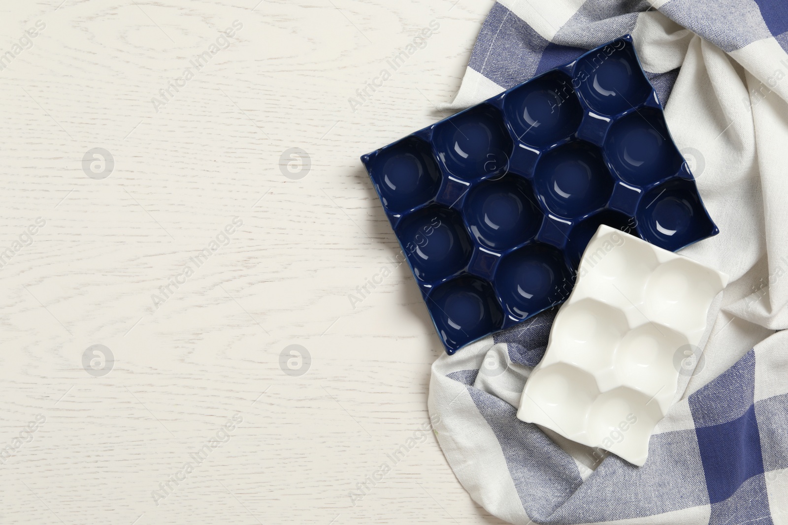 Photo of Cupcake trays and tablecloth on white wooden background, flat lay with space for text. Cooking utensils