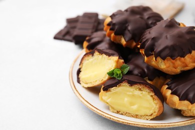 Photo of Delicious profiteroles with chocolate spread and cream on white table, closeup. Space for text