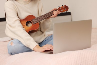 Photo of Woman with ukulele watching online music course via laptop at home, closeup. Time for hobby