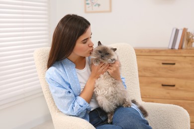 Woman kissing her cute cat on soft armchair at home