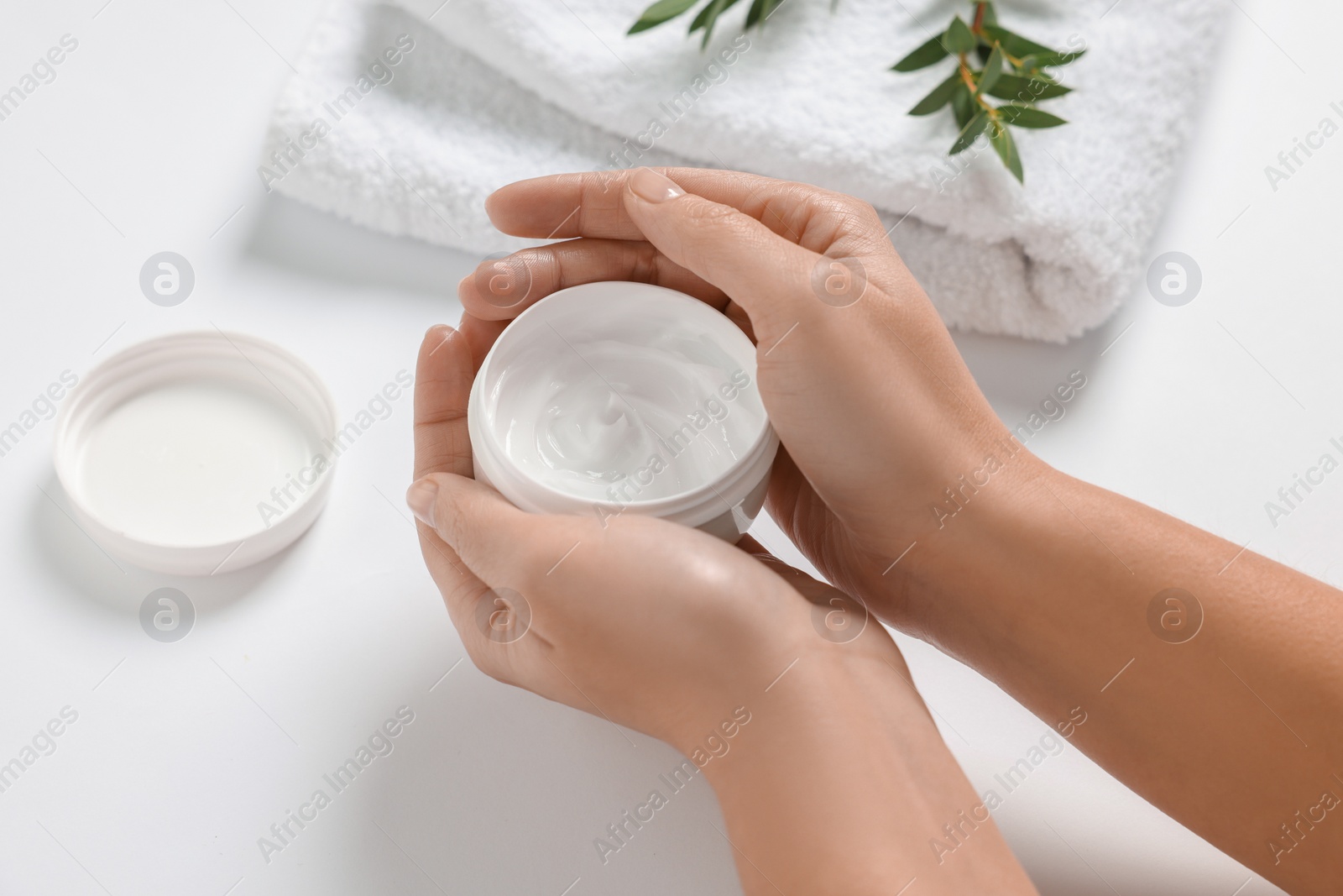 Photo of Woman with jar of hand cream, towel and green leaves on white background, closeup