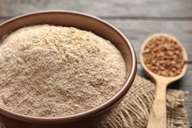 Image of Buckwheat flour in bowl and spoon with seeds on wooden table, closeup