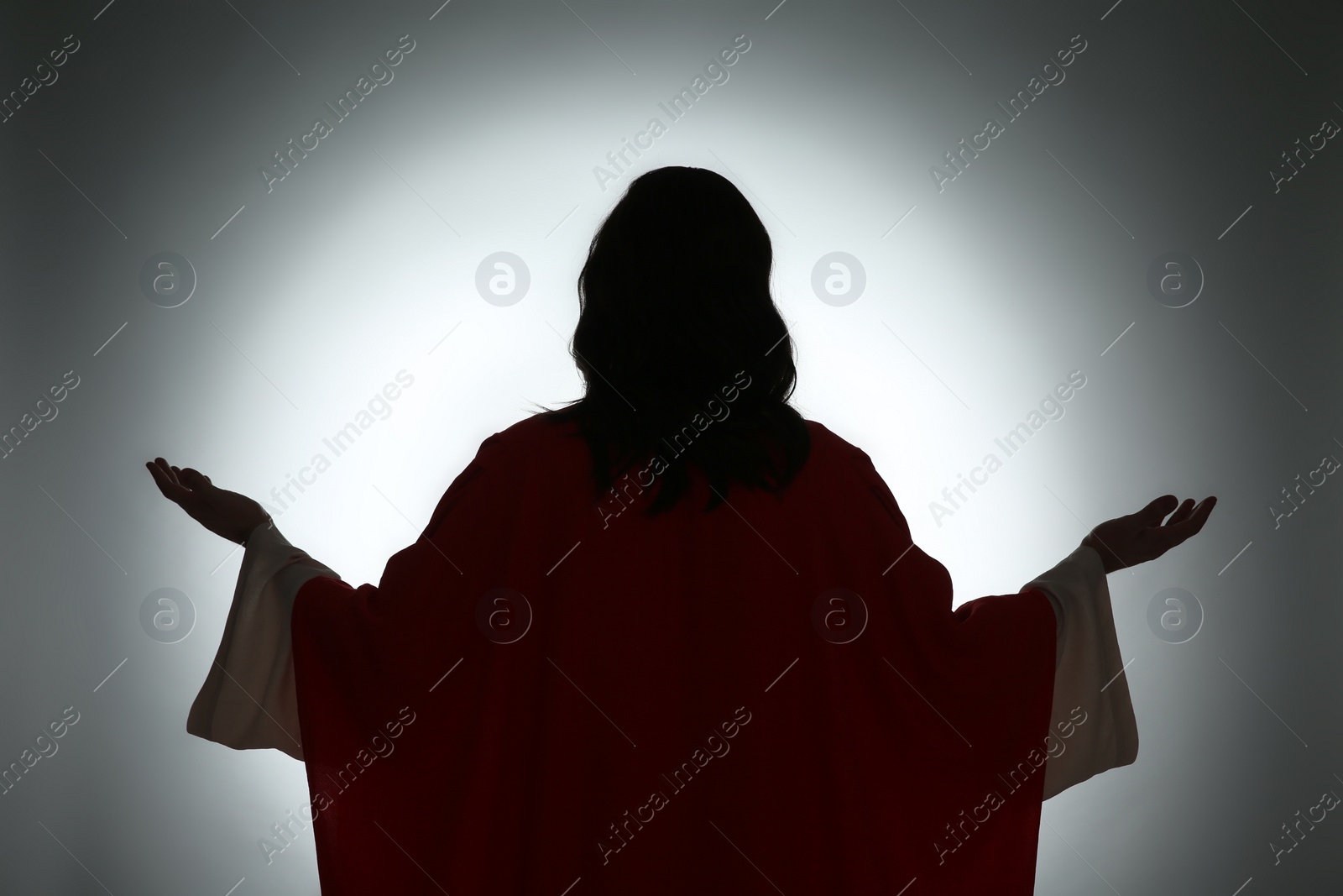Photo of Silhouette of Jesus Christ with outstretched arms on color background, back view