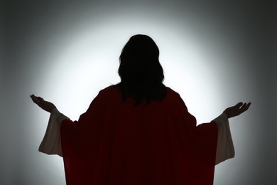 Photo of Silhouette of Jesus Christ with outstretched arms on color background, back view