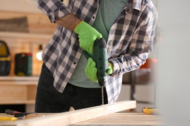 Photo of Carpenter working with electric drill at table indoors, closeup