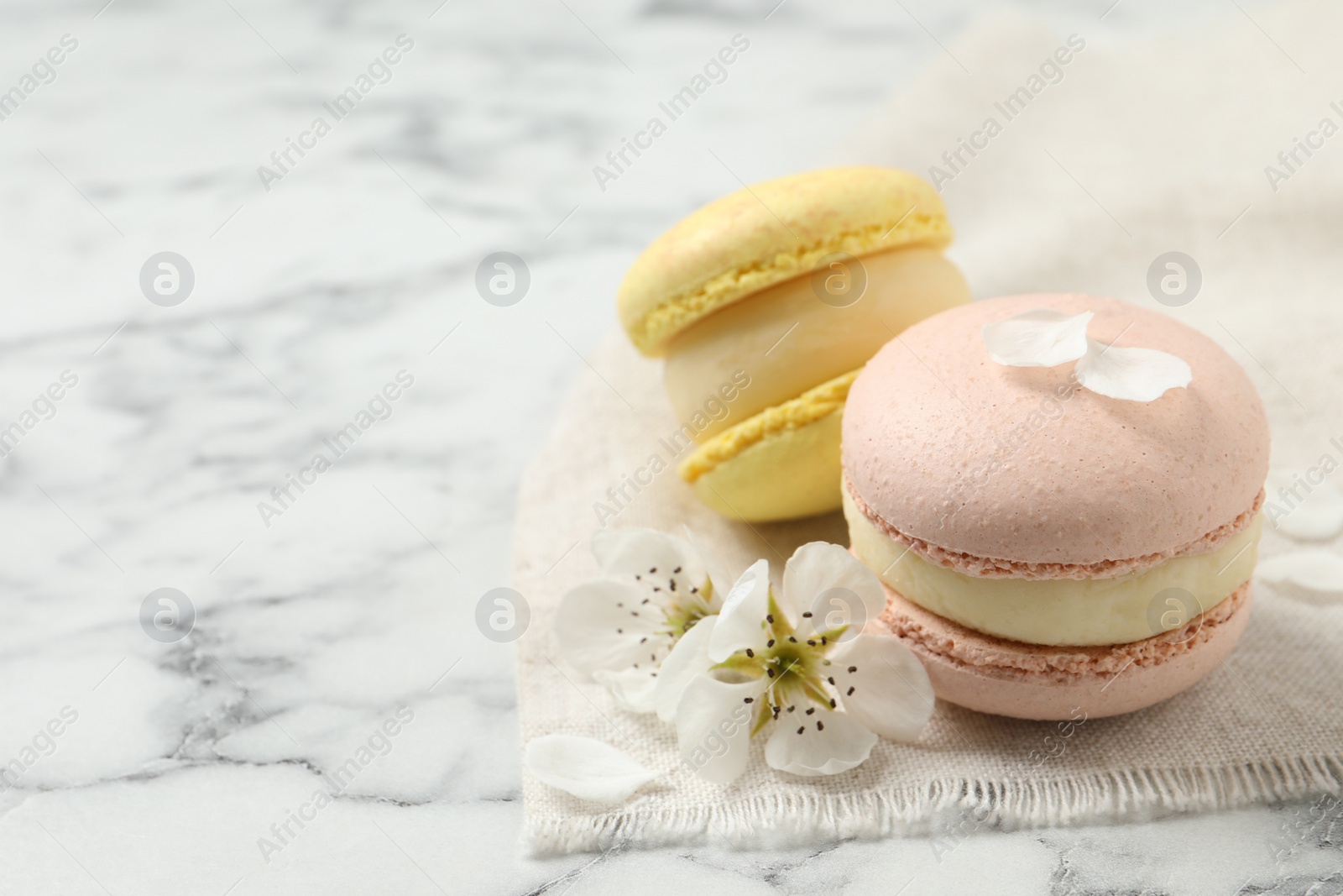 Photo of Delicious colorful macarons and flowers on white marble table. Space for text
