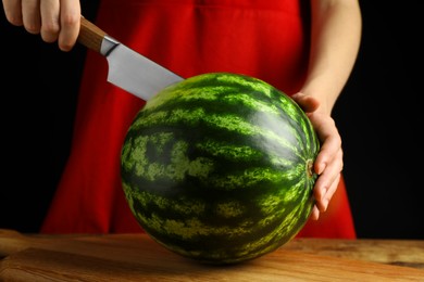 Photo of Woman cutting delicious watermelon at wooden table against black background, closeup