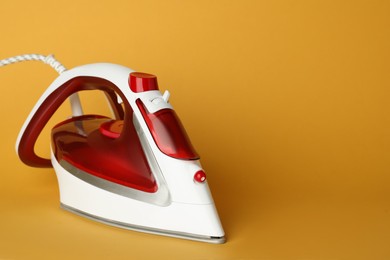 Photo of One modern iron on orange background, space for text. Home appliance