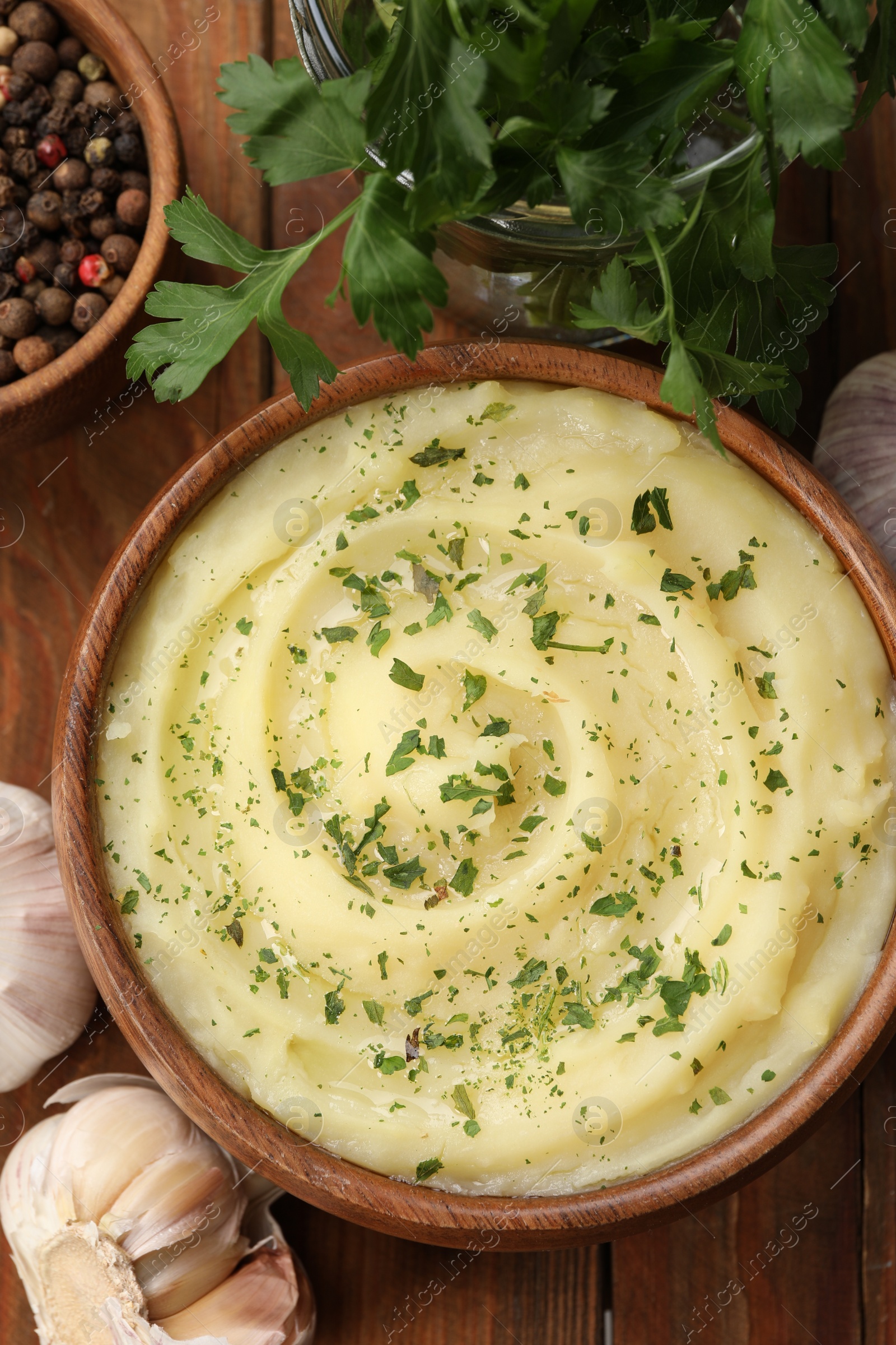Photo of Bowl of tasty mashed potato with parsley, garlic and pepper on wooden table, flat lay